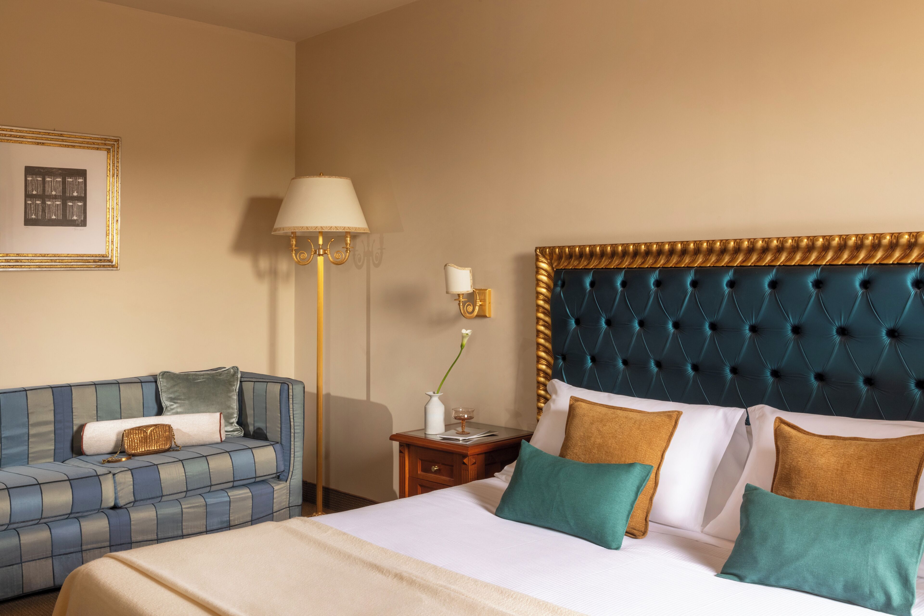 A hotel room with a bed, a sofa, a nightstand, a lamp, and a framed picture on the wall.