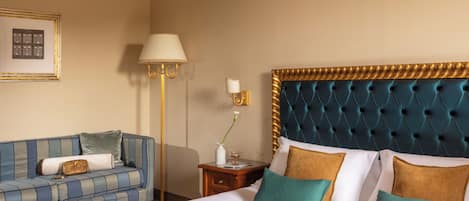 Quarto de hotel com uma cama, um sofá, uma mesinha de cabeceira, uma luminária e um quadro na parede.