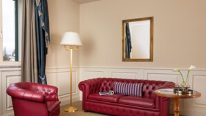 Un fauteuil en cuir rouge, un canapé rouge avec un coussin à rayures, une lampe sur pied, une table ronde en bois avec un vase, et un miroir au mur.