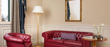 Ein rotes Ledersessel, ein rotes Sofa mit gestreiftem Kissen, eine Stehlampe, ein runder Holztisch mit einer Vase und ein Spiegel an der Wand.