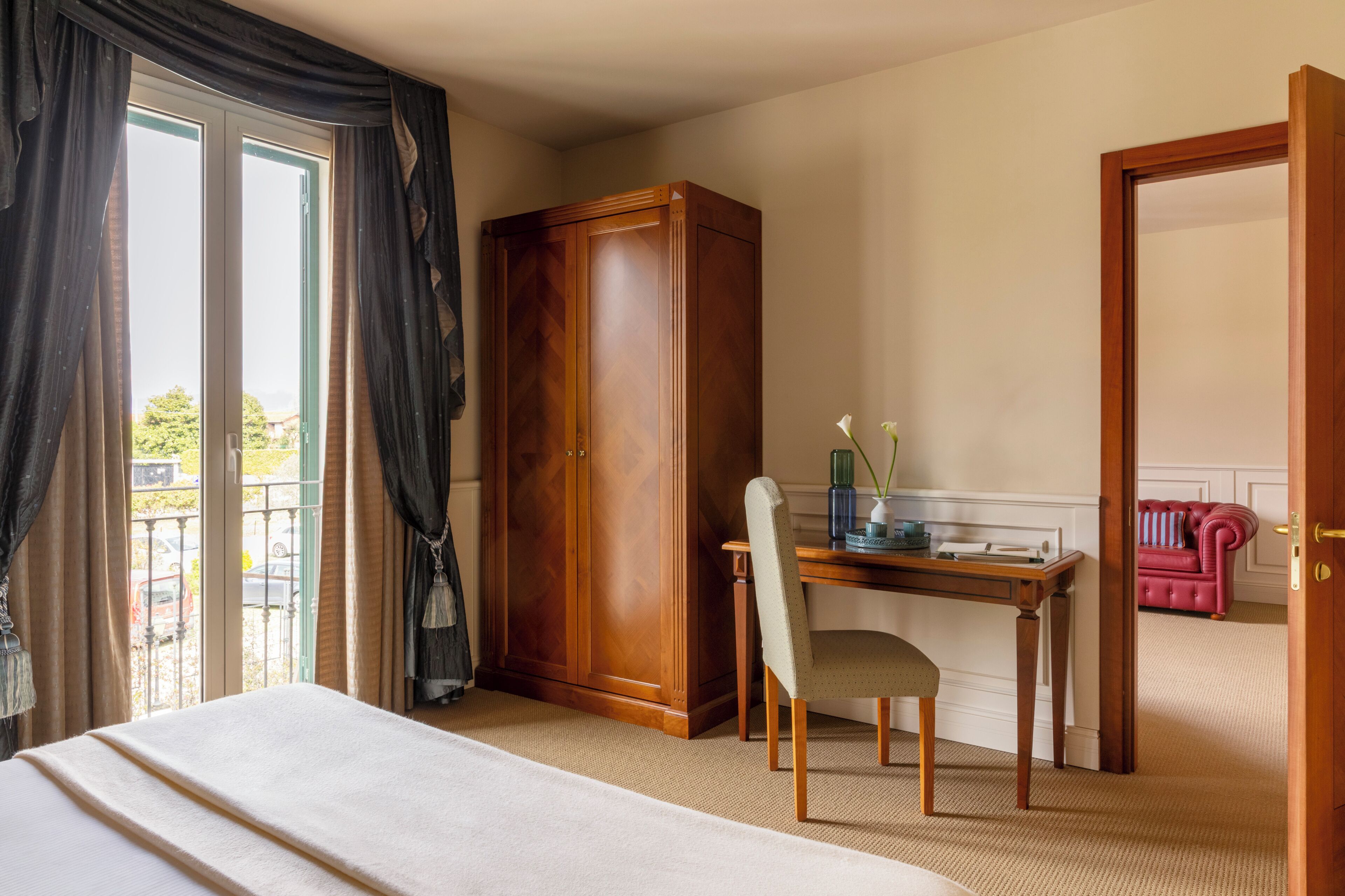A hotel room with a bed, a desk, a chair, a wardrobe, and a door leading to another room.