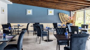 Un restaurant avec des chaises à l’assise rembourrée en bleu foncé, des tables en bois et un mur bleu orné d’œuvres d’art encadrées.