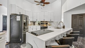 A modern kitchen with white cabinets, a stainless steel refrigerator, a built-in oven, a gas range, and a ceiling fan. - Relaxing Family Retreat In The Heart Of Sebastian 3 Bedroom Home (Sebastian)