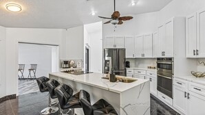 A modern kitchen with white cabinets, a central island with bar stools, stainless steel appliances, and a ceiling fan. - Relaxing Family Retreat In The Heart Of Sebastian 3 Bedroom Home (Sebastian)
