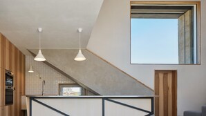 A modern kitchen with a central island, pendant lighting, and a large window above the staircase.