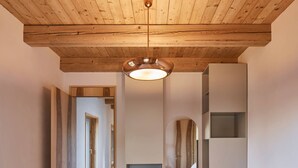 A bedroom with a wooden ceiling, a bed with white bedding, a bedside table with a lamp, and a mirror on the wall.