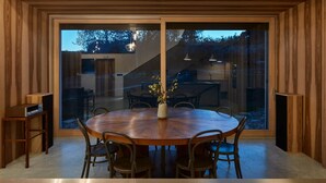 A modern dining area with a wooden table and chairs, large glass sliding doors, and a view of the outdoors.