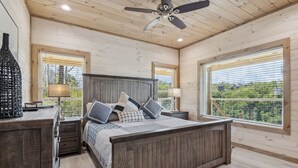 Quarto com cama de madeira, duas mesas de cabeceira, um ventilador de teto e janelas amplas com persianas.
