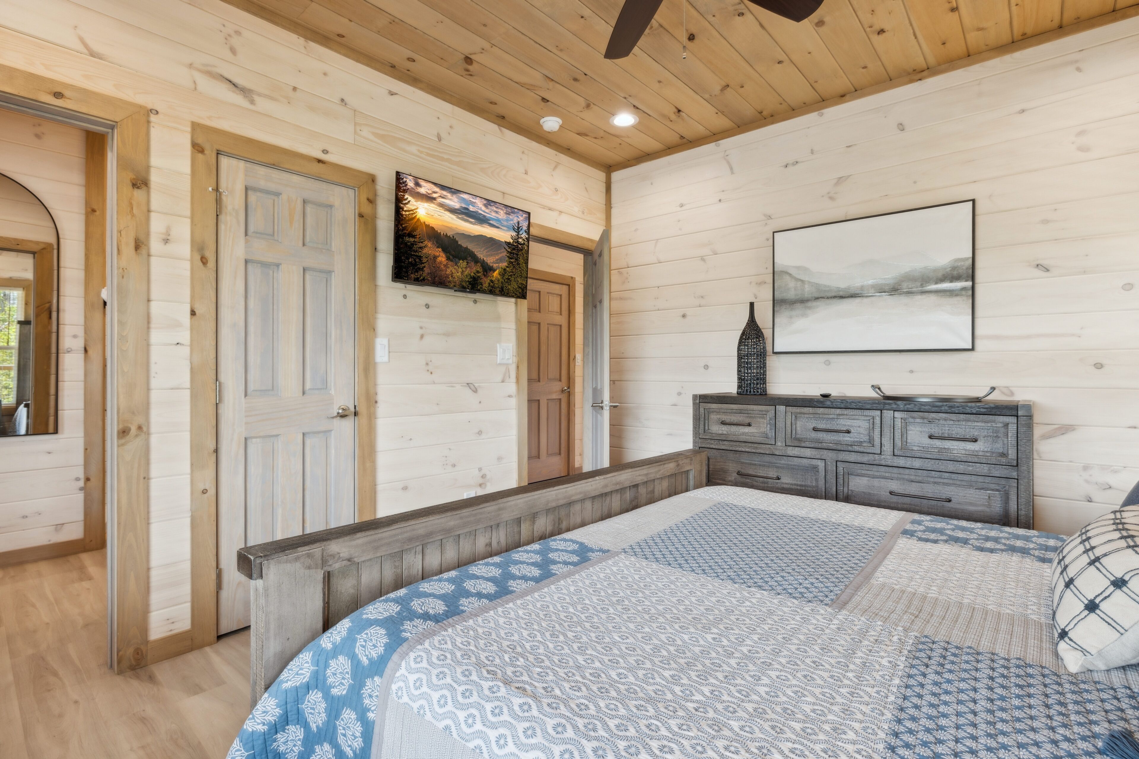 Ein Schlafzimmer mit Holzboden, einem Bett mit gemusterten Textilien, einem Schminktisch und zwei Türen.