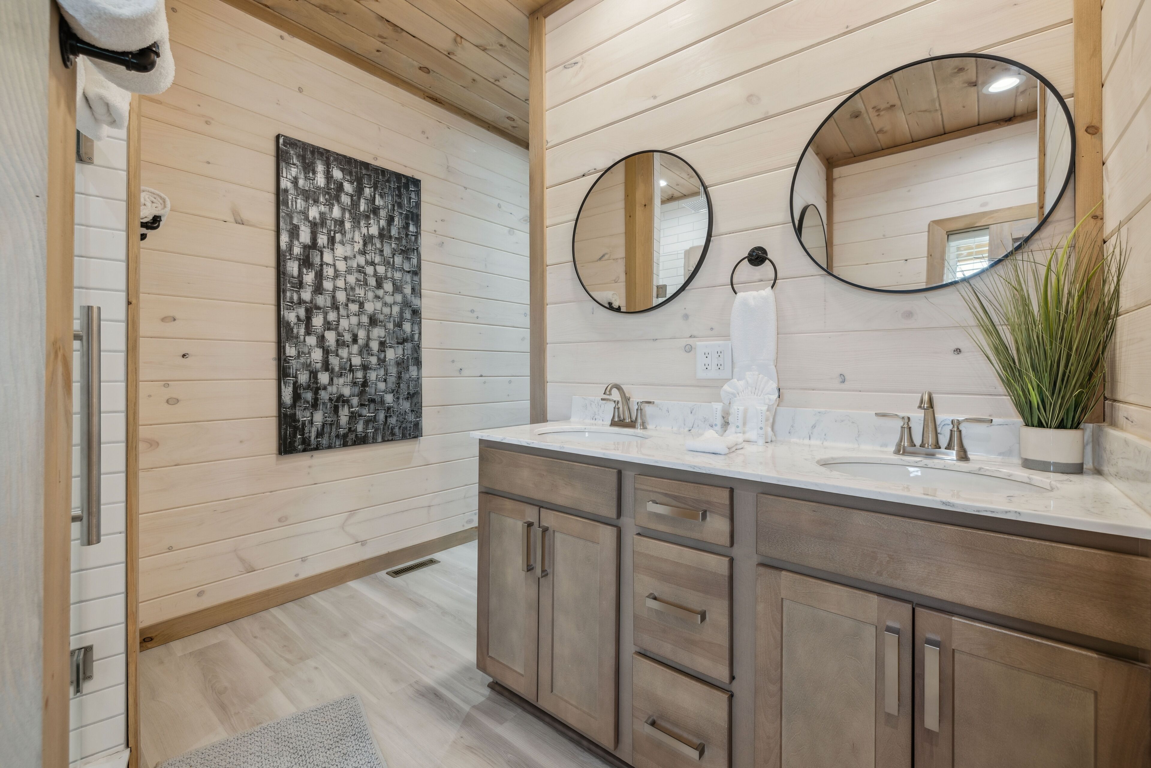 A modern bathroom with wooden panel walls, two sinks, and a large mirror.