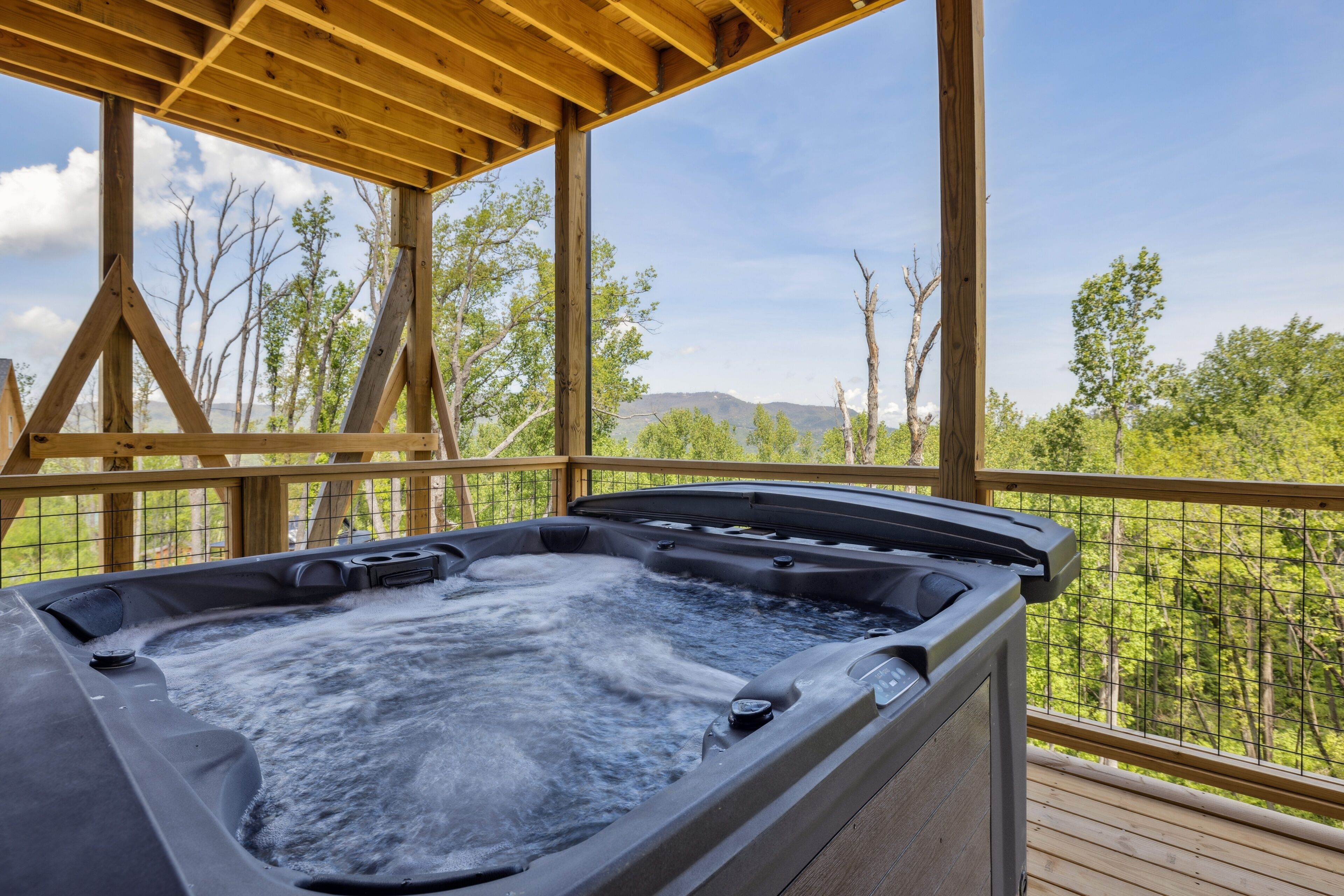 Een hottub op een houten terras met uitzicht op bomen en bergen.