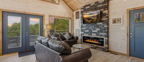 A spacious living room with a stone fireplace, a leather sofa, and a ceiling fan.