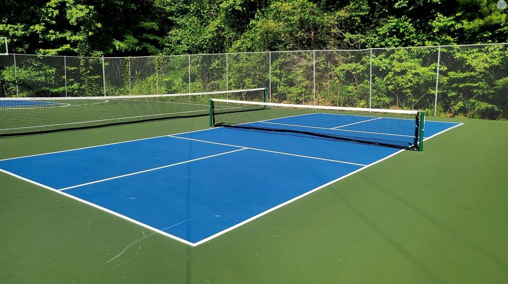 A tennis court with a net, surrounded by a chain-link fence and trees.