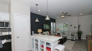 A modern kitchen with white cabinetry, a built-in microwave, and a stainless steel oven. There is a dining area with a white table and chairs, and a living room with a sofa and a coffee table. - Modern Ascend 2 Bedroom Townhouse (Grand Junction)
