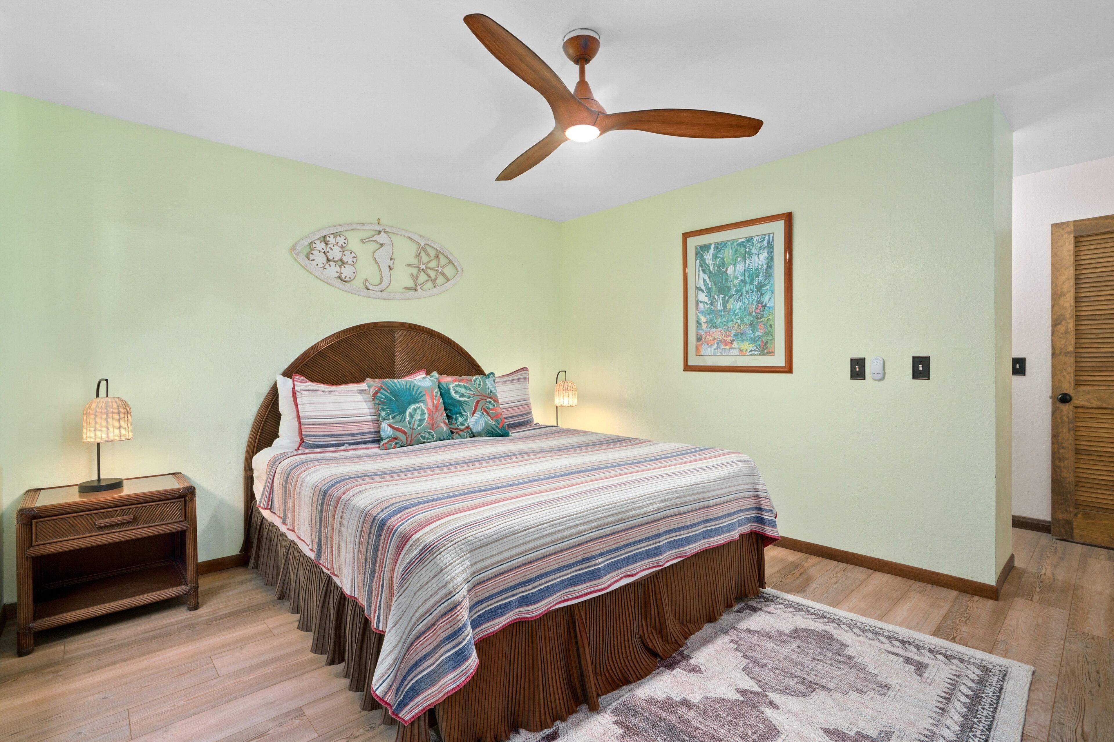 Un dormitorio con cama, mesita de noche, ventilador de techo, reloj de pared y puerta.