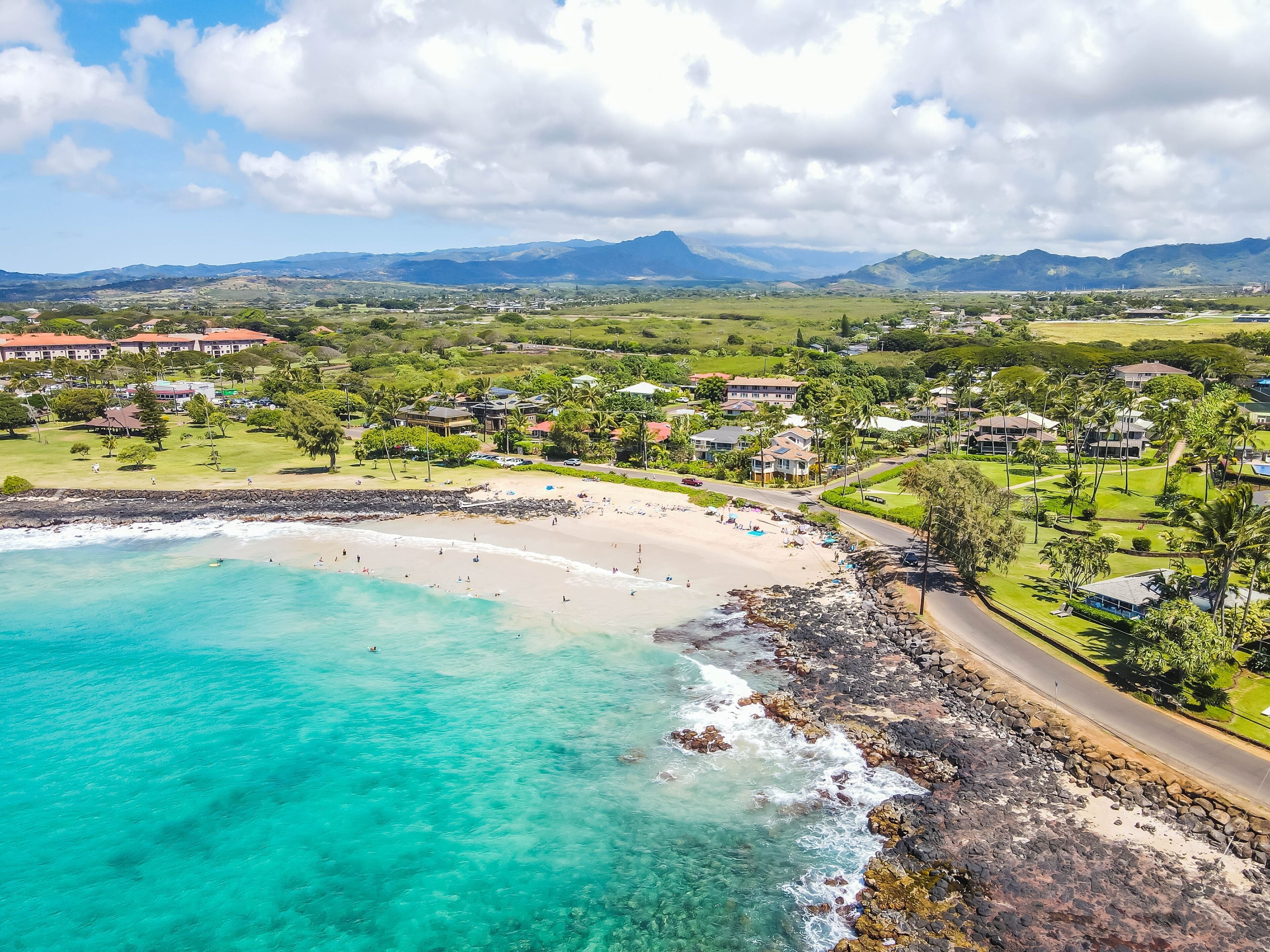 Uma vila costeira com uma praia, casas e montanhas ao fundo.