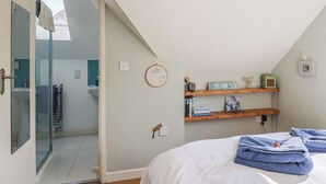 A bedroom with a bed, a wooden shelf with books and a clock, and a bathroom visible through an open door. - Bentley Rise (Lyme Regis)