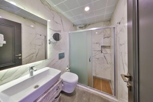 A modern bathroom with a marble vanity, a toilet, and a glass-enclosed shower.
