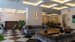 A modern lobby with a checkered floor, a grey sofa, a wooden coffee table, and a large potted plant. - Brow City Kaş (Kas)