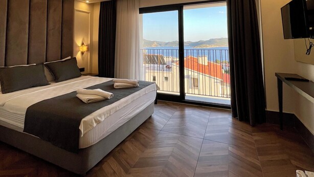A modern hotel room with a large bed, a TV, and a balcony with a view of the sea. - Brow City Kaş (Kas)