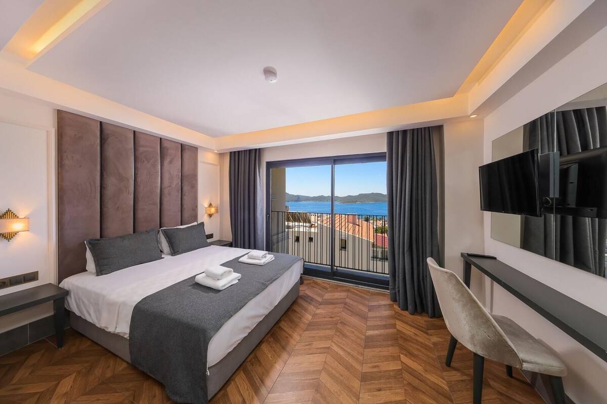 A hotel room with a bed, a desk, a chair, a TV, and a balcony with a view of the sea.