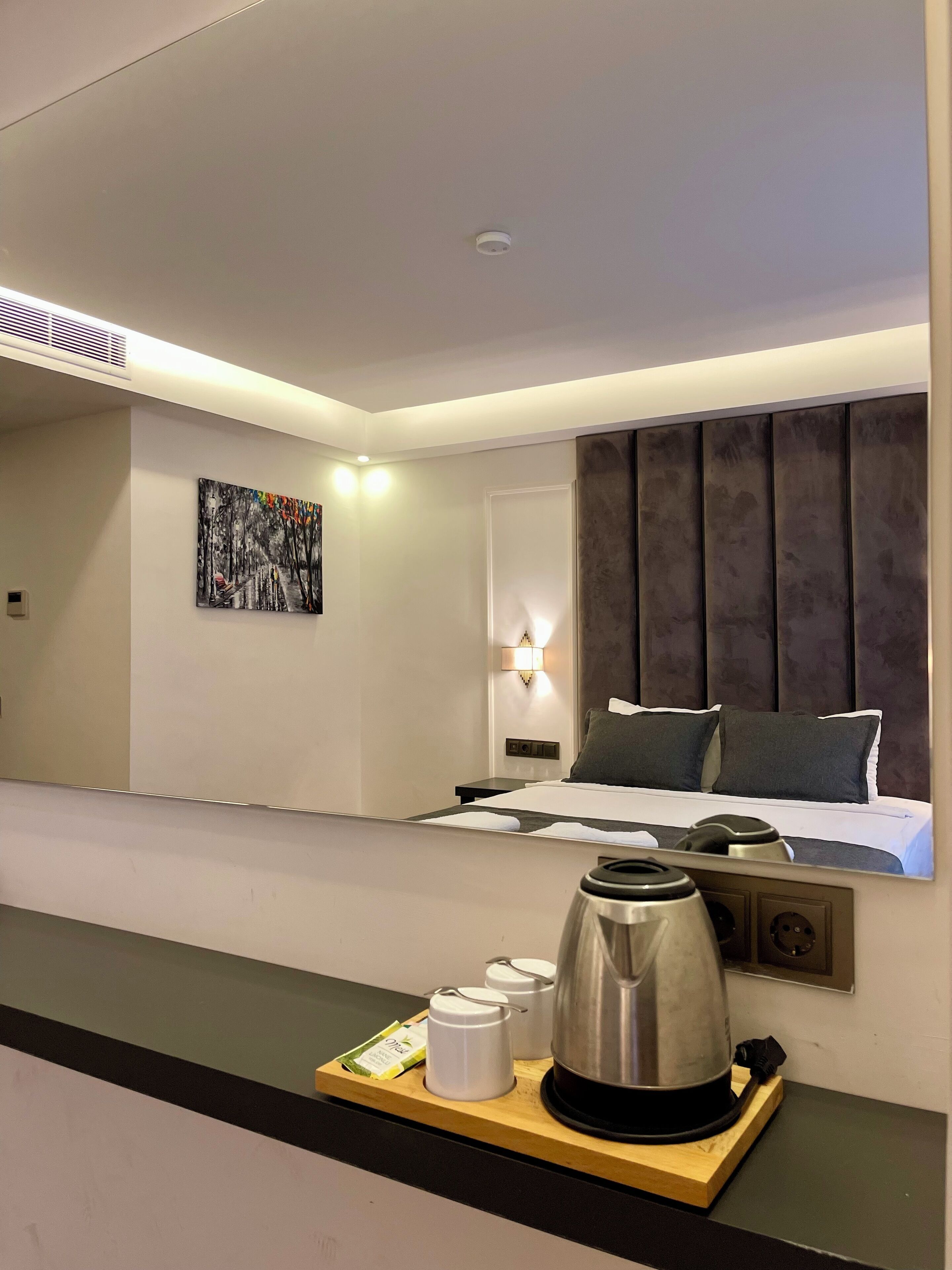 A hotel room with a bed, bedside table, wall-mounted lamp, and a painting on the wall.
