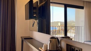 A hotel room with a modern kitchenette, a large window with a view of the city, and a flat-screen TV mounted on the wall. - Brow City Kaş (Kas)