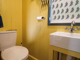 Un baño con una pared amarilla, un inodoro blanco, un lavamanos blanco y una toalla colgada en la pared.