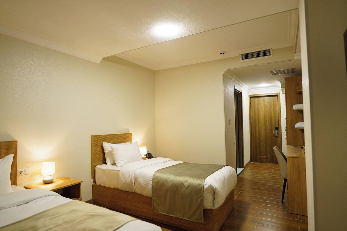 Een hotelkamer met twee bedden, een houten hoofdbord, een nachtkastje met een lamp en een bureau met een stoel.