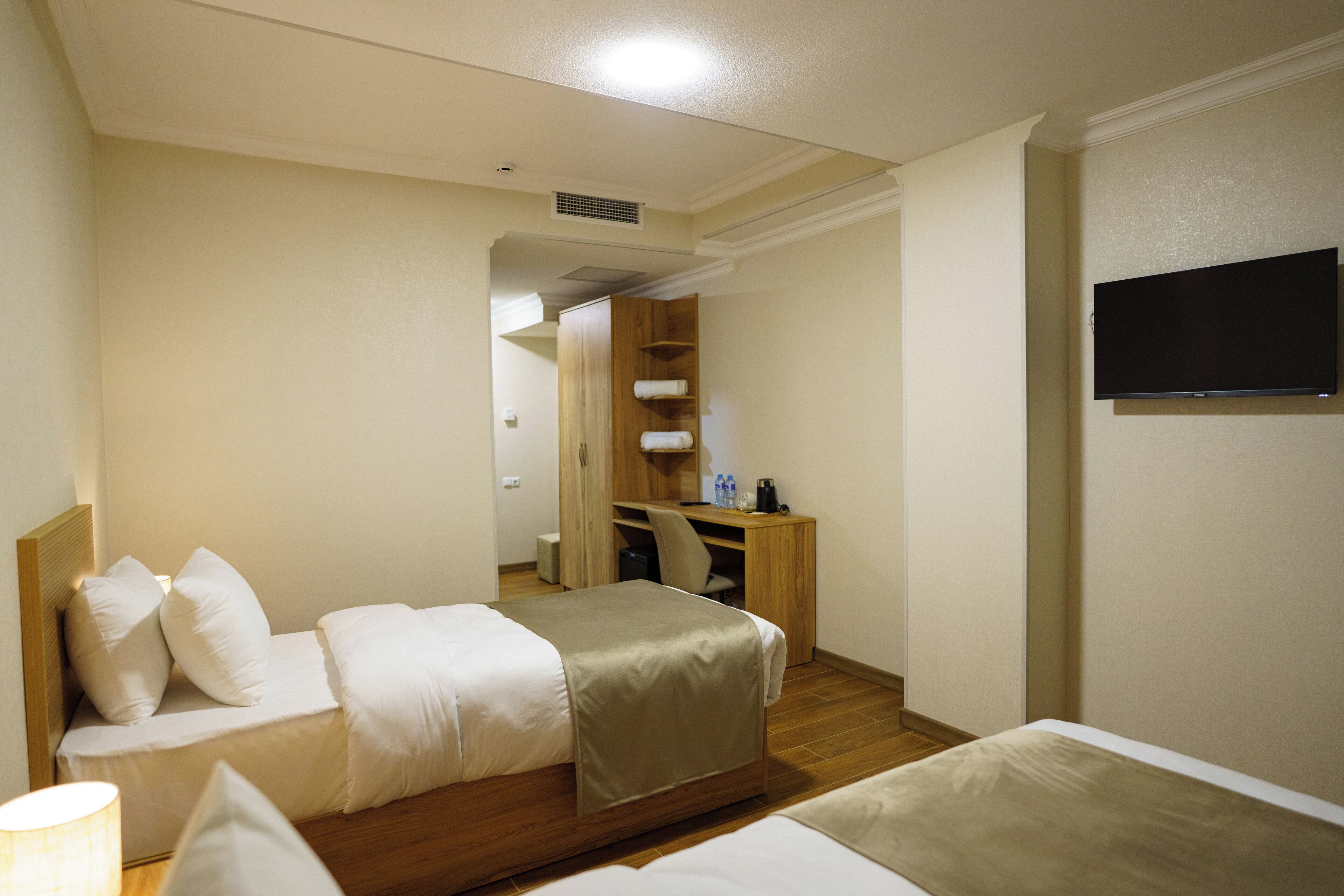 Ein Hotelzimmer mit zwei Betten, einem Schreibtisch, einem Fernseher und einem begehbaren Kleiderschrank.