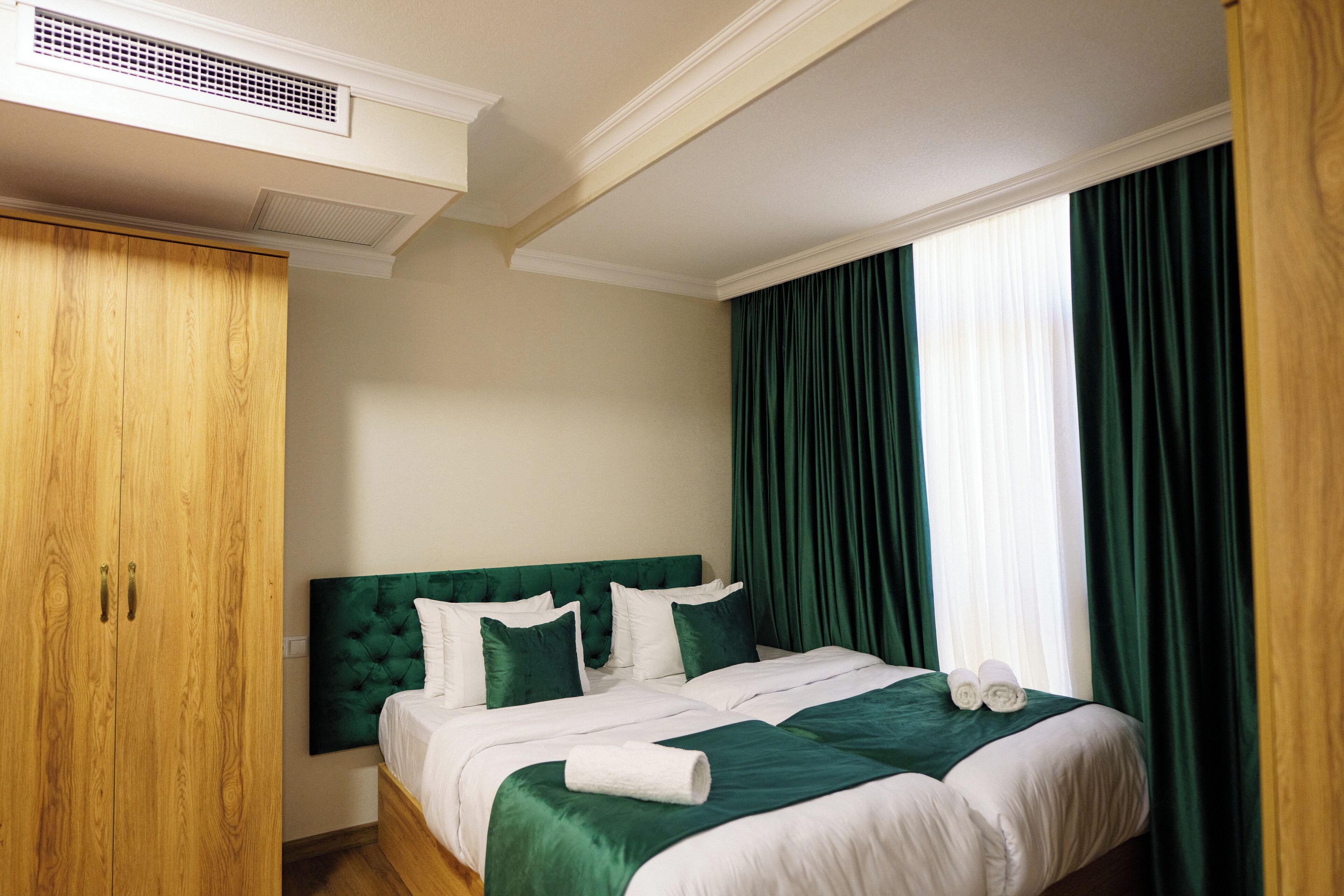 A hotel room with a large bed, green curtains, and a wooden wardrobe.