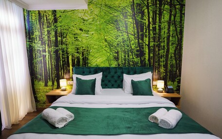 A hotel room with a large bed, green bedding, and a forest-themed wall mural.