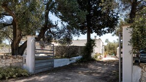 Una entrada tancada amb una paret de pedra, una reixa de metall i un camí cap a un edifici.