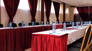 Une salle de conférence avec une longue table, des rideaux rouges et des bouteilles d’eau posées sur la table.