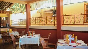 Un restaurant avec des tables dressées pour le service, des chaises en bois et une vue sur la rue, visible à travers une fenêtre ornée d’une grille en métal.