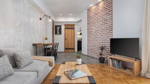 A modern living room with a sofa, coffee table, TV, bookshelf, and a brick wall. - Acropolis Atmospheric Apartment (Athens)