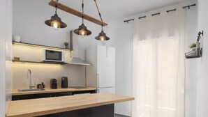 A modern kitchen with a wooden countertop, stainless steel sink, and a microwave. There are pendant lights, a refrigerator, and a window with sheer curtains. - Acropolis Atmospheric Apartment (Athens)