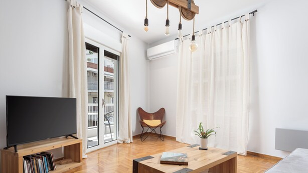 A modern living room with a flat-screen TV, wooden coffee table, and a comfortable chair. - Acropolis Atmospheric Apartment (Athens)