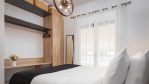 A modern bedroom with a large bed, wooden paneling, a hanging light fixture, and a view through sheer curtains. - Acropolis Atmospheric Apartment (Athens)