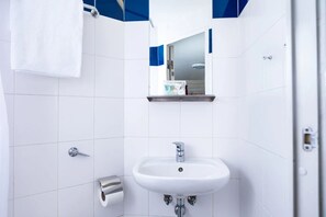 Un bagno con piastrelle bianche, un lavandino bianco, uno specchio, un porta asciugamani e un portasciotto.