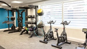 Un gimnasio con equipo de levantamiento de pesas, kettelbells y bicicletas estáticas.