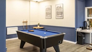 Una mesa de billar en una habitación con paredes azules y techo blanco. Hay dos cuadros en la pared.