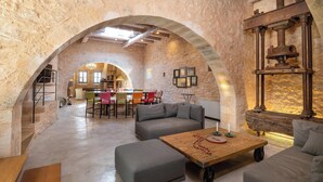 Un intérieur spacieux agrémenté d’une arche en pierre menant à un coin repas, d’un espace salon confortable avec une table basse et d’un mur rustique orné d’un élément décoratif aquatique.