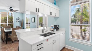 A kitchen with white cabinets, a double sink, and a dining area with wicker chairs.