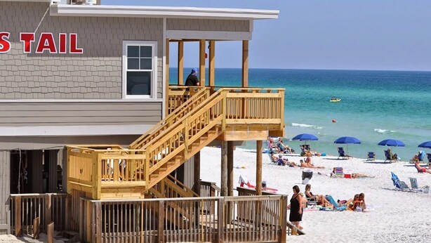 A beachside building with a lifeguard tower, wooden deck, and beach umbrellas.