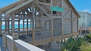 A wooden beach house named 'Emerald Shores' with a covered deck and a view of the ocean.