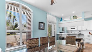 A dining area with a glass table, woven chairs, and a view through large windows.