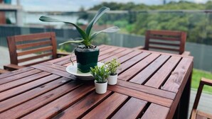 Una mesa de madera con plantas en macetas, vista a follaje y una estructura distante.