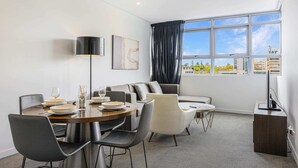 A modern living room with a dining area, large windows, and a view of the city. - Prime Location 1BD Apartment in Chatswood (Chatswood)
