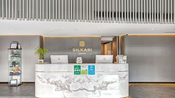 A hotel reception desk with a marble top, two HP laptops, a plant, and a sign reading "Silkari Suites".